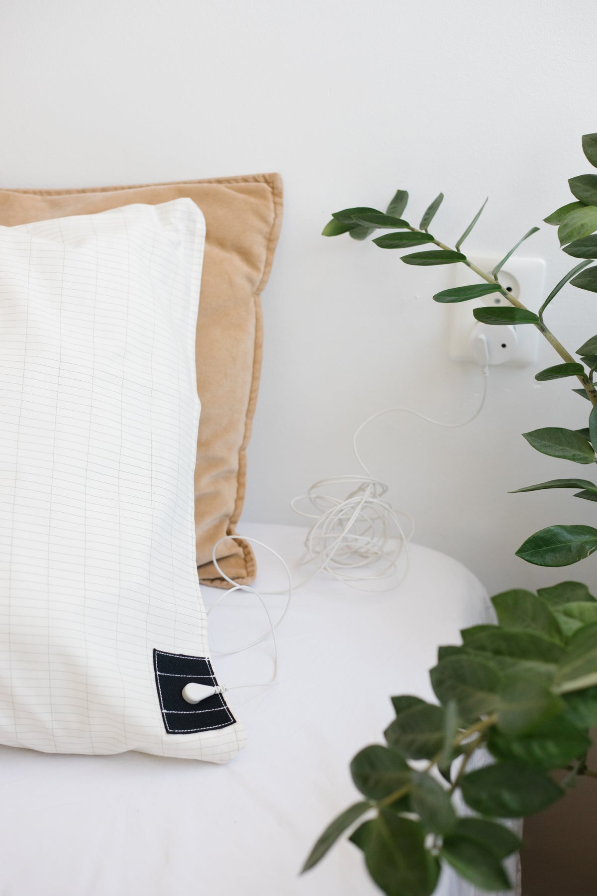 Earthle aardingskussensloop om een hoofdkussen op een opgemaakt bed, met een kamerplant ernaast