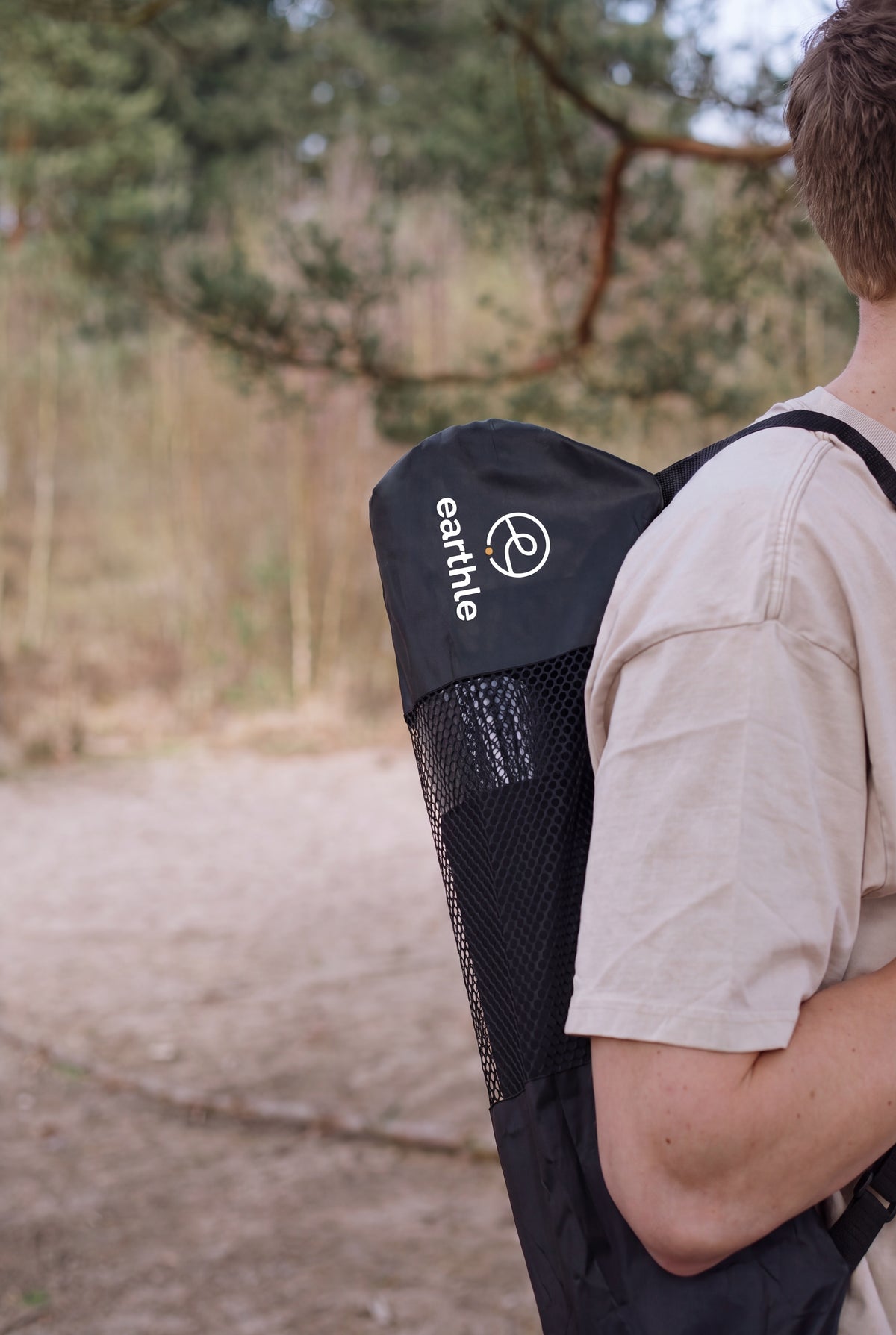 Iemand draagt de Earthle aardingsyogamat in de draagtas op de rug, buiten in het bos