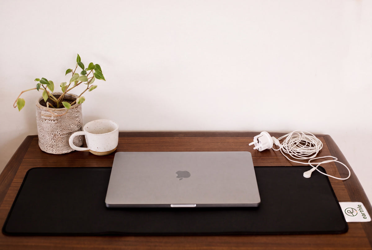 Earthle aardingsbureaumat op een bureau met laptop, plant en beker, kabel naar het stopcontact